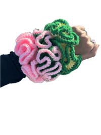 a woman's hand holding a pink and green crocheted cuff