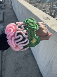 a person holding a crocheted bracelet with pink and green flowers